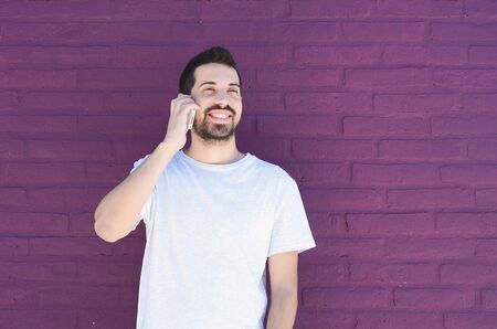 Portrait of young latin man talking on the phone against brick wall. Outdoors.の写真素材