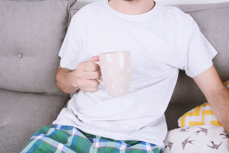 Attractive young man drinking coffee and relaxed on couch. Indoors.の写真素材