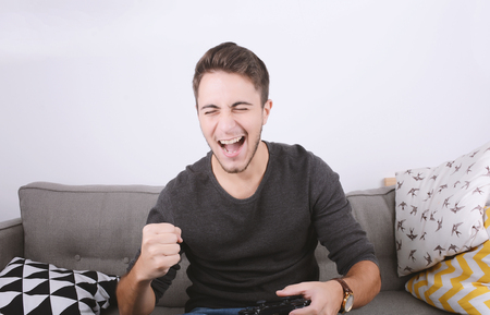 Portrait of young man playing videogames and sitting on couch. Indoors.の写真素材