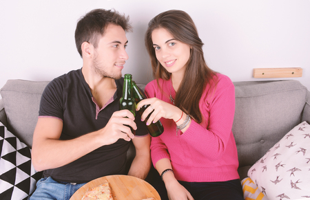 Beautiful young couple drinking beer and eating pizza. Indoors.の写真素材