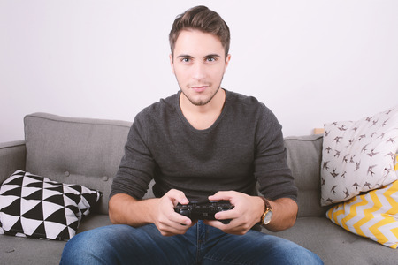 Portrait of young man playing videogames and sitting on couch. Indoors.