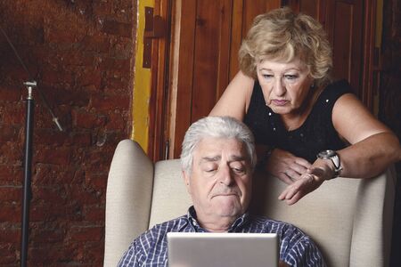 Portrait of an old couple using digital tablet sitting on couch. Indoors.