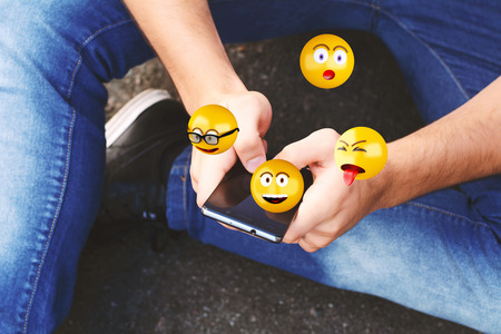 Close-up of man using smartphone sending emojis. Social concept.