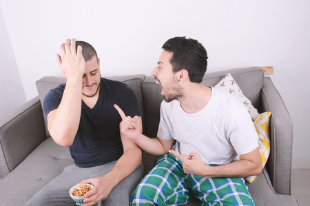 Portrait of two friends playing videogames and sitting on couch. Indoors.の写真素材