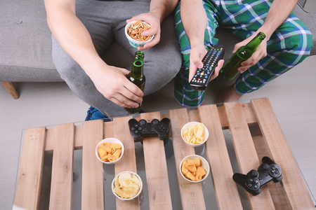 Portrait of two friends playing videogames, eating snacks and drinkng beer. Indoors.の写真素材