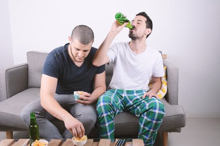Two friends eating snacks and drinking beer. Indoors.の写真素材
