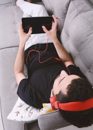 Attractive young man listening to music with digital tablet on couch. Indoors.の写真素材