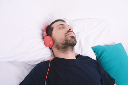 Attractive young man listening to music and relaxed in bed. Indoors.の写真素材