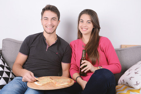 Beautiful young couple drinking beer and eating pizza. Indoors.の写真素材