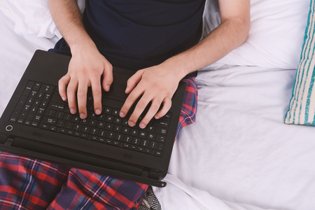 Attractive young man using his laptop in bed. Indoors.の写真素材