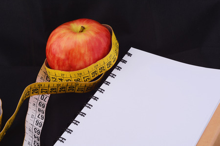 An apple and measuring tape on notepad. Healthy food concept. Isolated black background.の写真素材