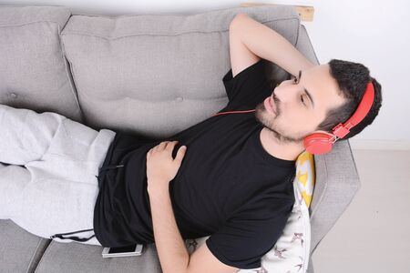 Attractive young man listening to music with headphones and relaxed on couch. Indoors.