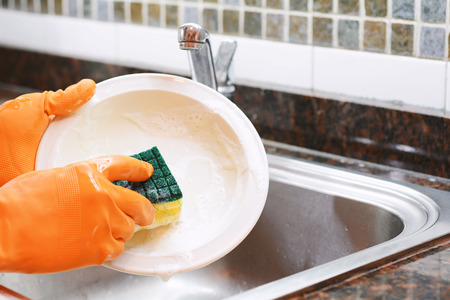 Close-up view of hands in rubber gloves washing dishes with sponge. Housework concept