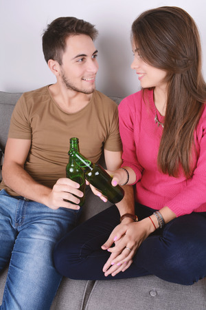 Beautiful young couple drinking beer and relaxed on couch. Indoors.の写真素材