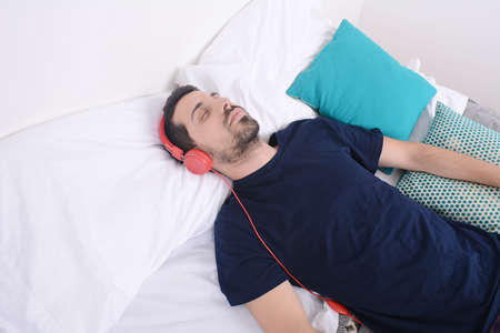 Attractive young man listening to music and relaxed in bed. Indoors.の写真素材