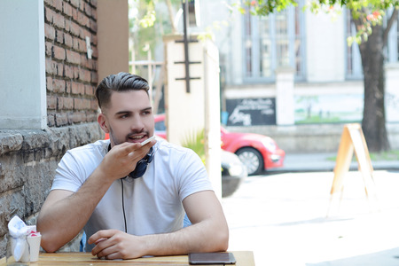 Portrait of young latin man sending voice messages. Outdoors. Urban scene.の写真素材