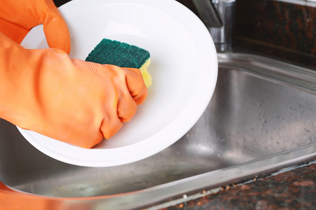 Close-up view of hands in rubber gloves washing dishes with sponge. Housework conceptの写真素材