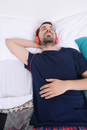 Attractive young man listening to music and relaxed in bed. Indoors.の写真素材