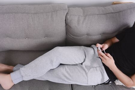 Attractive young man using his smartphone and relaxed on couch. Indoors.