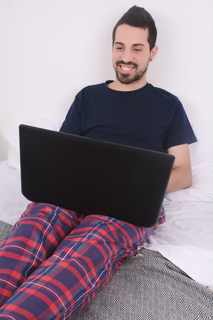 Attractive young man using his laptop in bed. Indoors.の写真素材