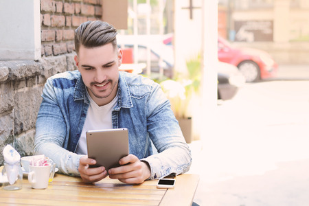 Young man in coffee shop cafe using a tablet. Outdoors