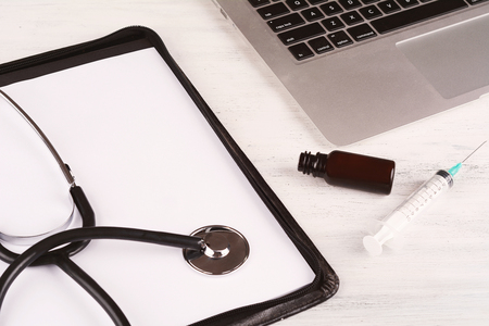 Top view of laptop, notepad, stethoscope, medicine bottles and syringe at doctor's desk. Modern medicine workplaceの写真素材