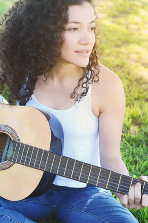 Outdoor portrait of a young beautiful latin woman playing guitar at the park.の写真素材