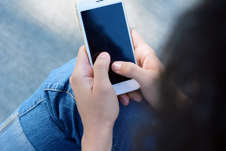 Close-up of woman hands holding and touching on blank black screen smartphone on the street.の写真素材