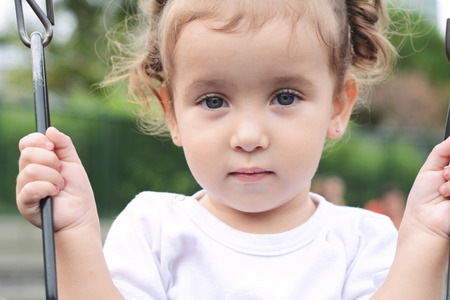 Cute little girl on a swing in the park. Summer portrait