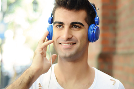 Portrait of young latin man listening to music with headphones. Outdoors.の写真素材