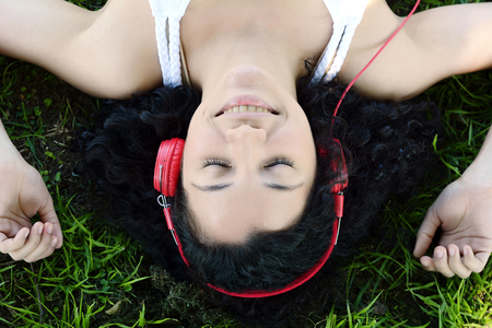 Portrait of young latin woman with headphones listening to music at the park in summer. Enjoying Music.の写真素材