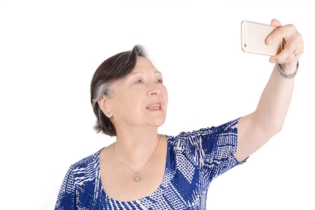 Beautiful senior woman with cellphone taking a selfie. Technology concept. Isolated white backgroundの写真素材