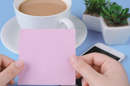 Woman's hand holding empty card with coffee and phone on a light blue background.の写真素材