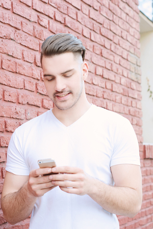 Portrait of young latin man typing on his phone. Outdoors.の写真素材