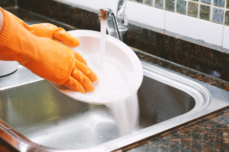 Close-up view of hands in rubber gloves washing dishes with sponge. Housework conceptの写真素材