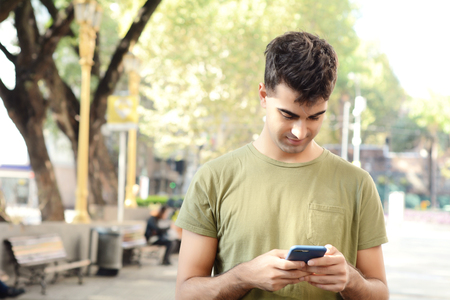 Portrait of young latin man typing on his phone. Outdoors.の写真素材