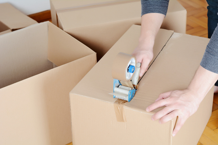 Man sealing a shipping cardboard box with tape dispenser. Indoorsの写真素材