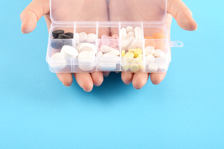 Close up of hand showing medicine box with pills on Blue background