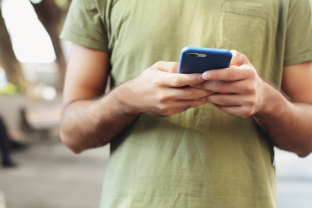 Portrait of young latin man typing on his phone. Outdoors.