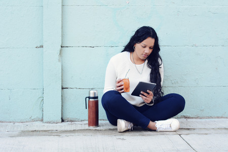 Portrait of Young latin woman drinking traditional Argentinian yerba mate tea with tablet. South...