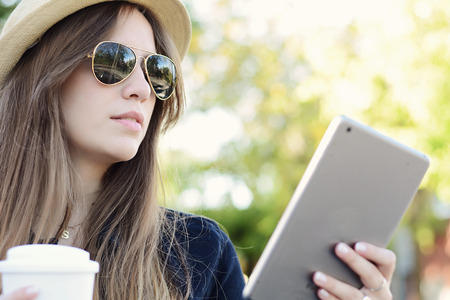 Portrait of a young beautiful woman using her tablet with coffee cup. Outdoors. Urban scene.