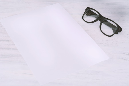Empty paper with glasses on white wooden background