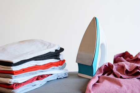 Close up view of iron clothes on ironing board with stack of ironed shirts. Housework conceptの写真素材