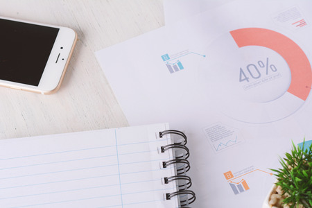 Close up of phone, spiral notepad and financial papers with charts and numbers. Business conceptの写真素材