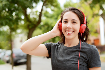 Portrait of young beautiful woman with red headphones listening music. Outdoors. Urban concept.の写真素材