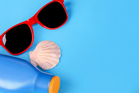 Top view of sunglasses, shells, starfish and sunblock with copyspace. Summer concept. Light blue...