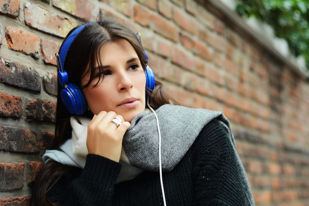 Portrait of young latin woman with blue headphones against a wall.の写真素材