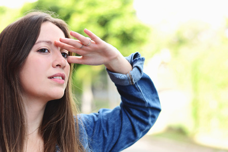 Portrait of young hispanic woman looking far with hand at her forehead, summer outdoors.