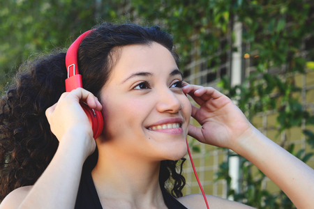 Portrait of young latin woman with headphones listening to music at the park in summer. Enjoying Music.の写真素材