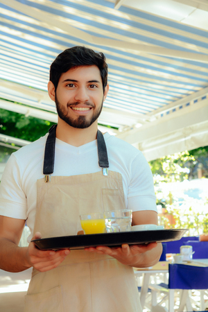 Handsome young waiter holding tray at the coffee shop. Service conceptの写真素材